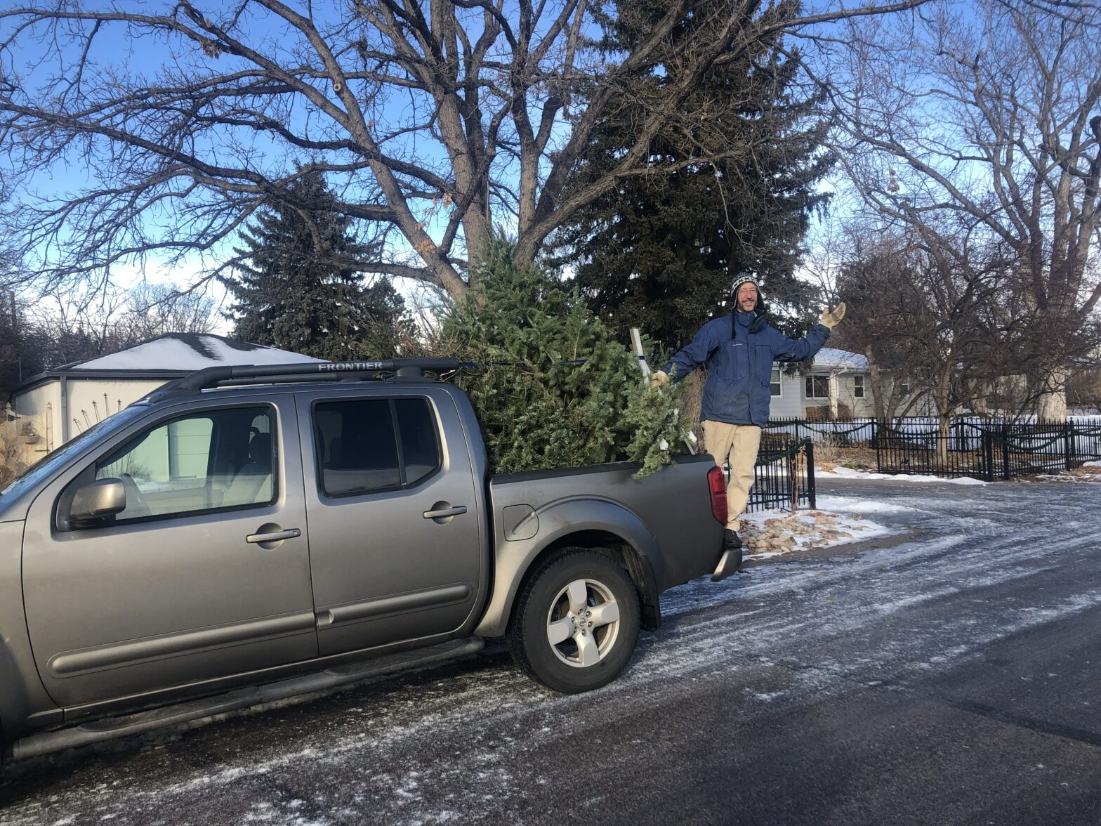 Adam riding on the back of a pickup truck full of Christmas trees.